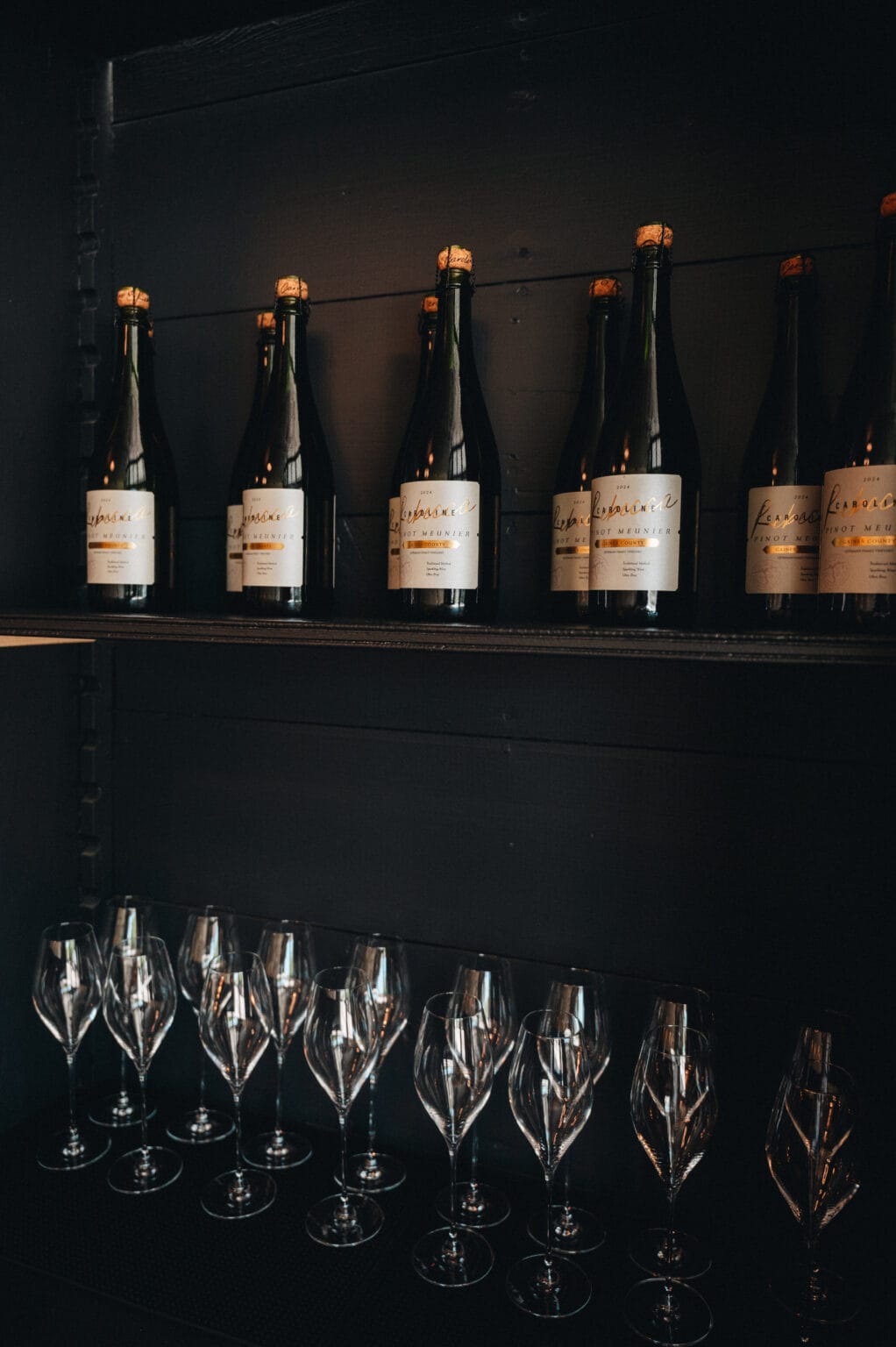 Bottles lined on a dark ledge above rows of waiting flutes in the lounge