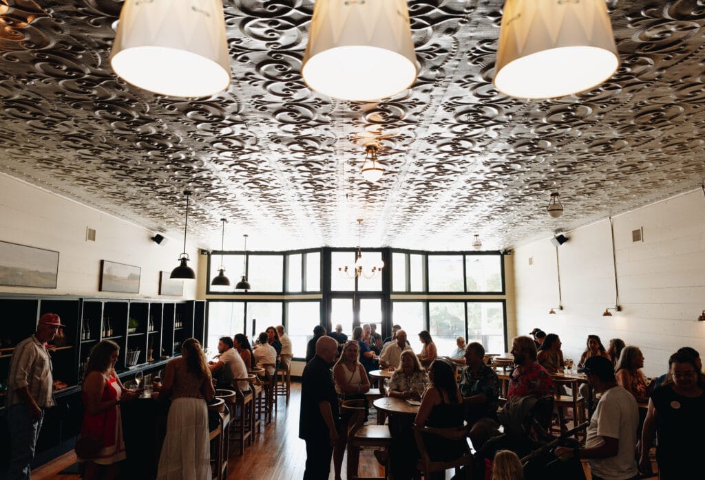 The Rebecca Caroline tasting room under its pressed-tin ceiling and globe lights, full of guests