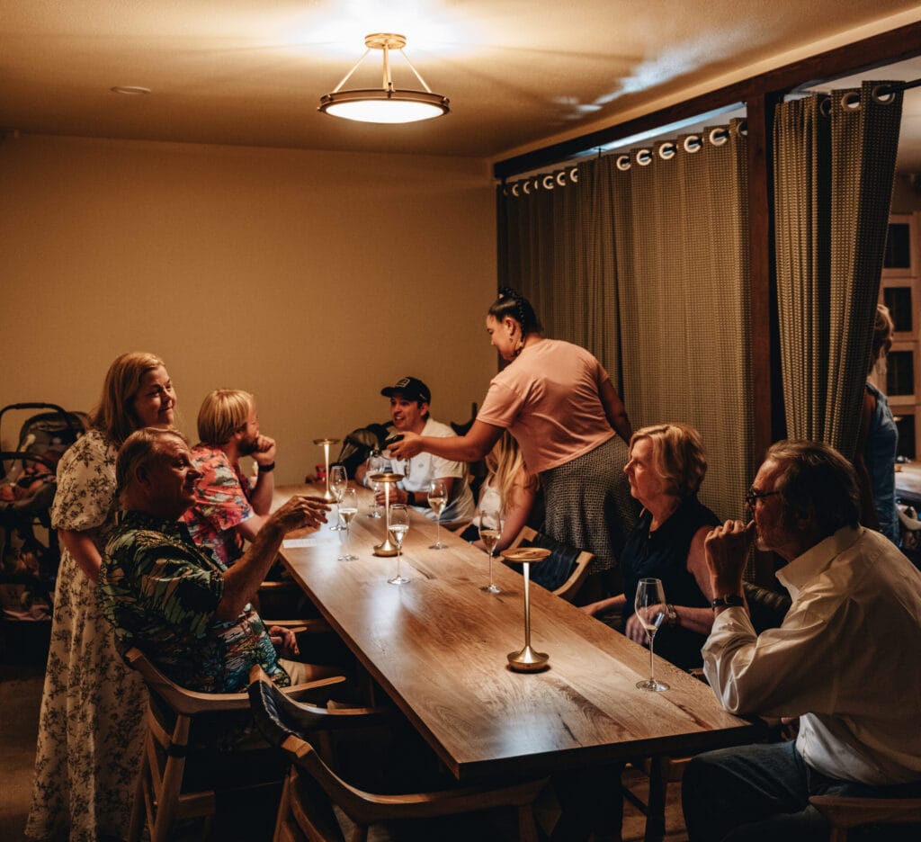 Guests seated along the communal table in the member's lounge in low lamplight
