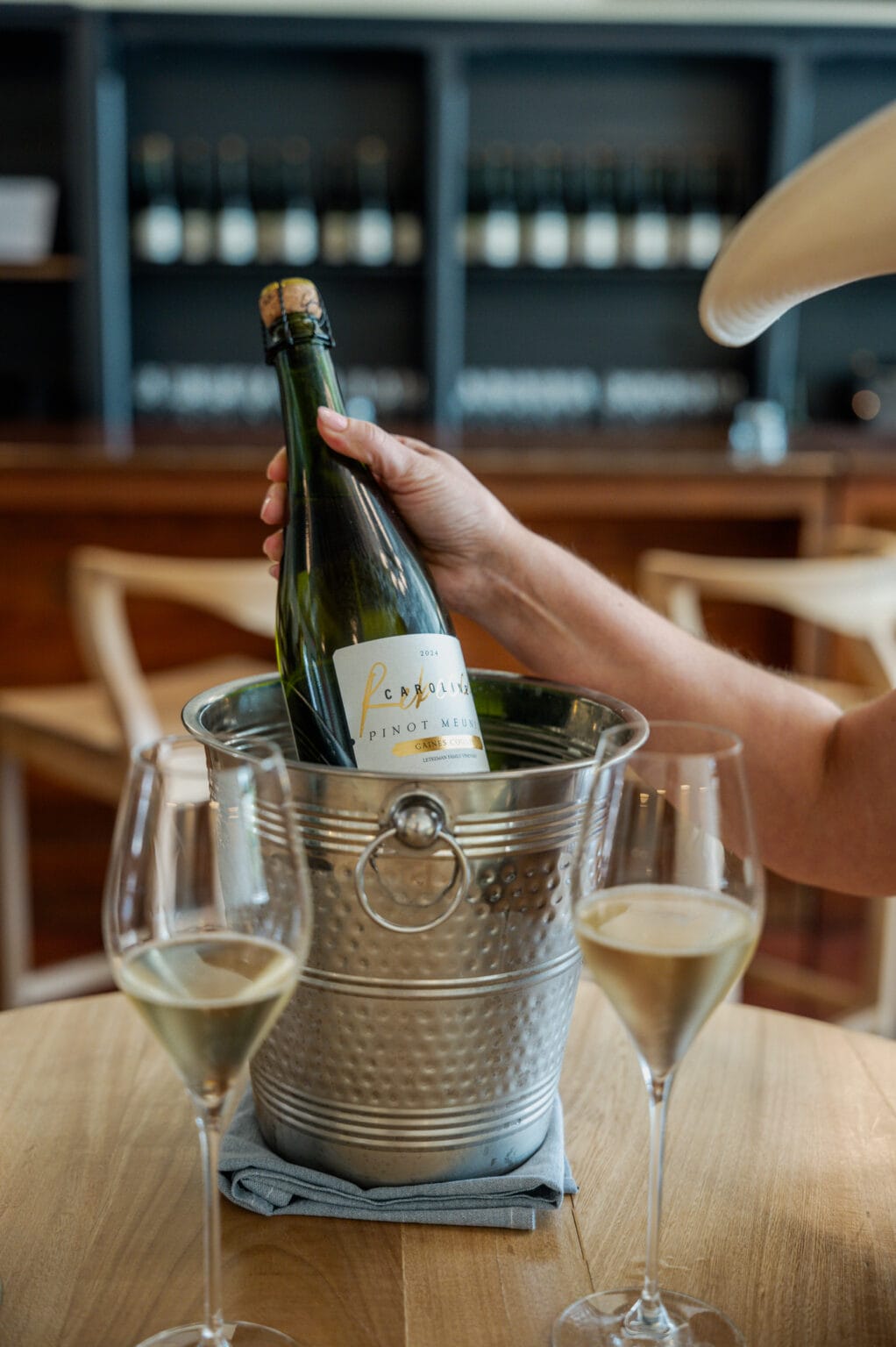 A bottle of Rebecca Caroline chilling in an ice bucket beside poured glasses