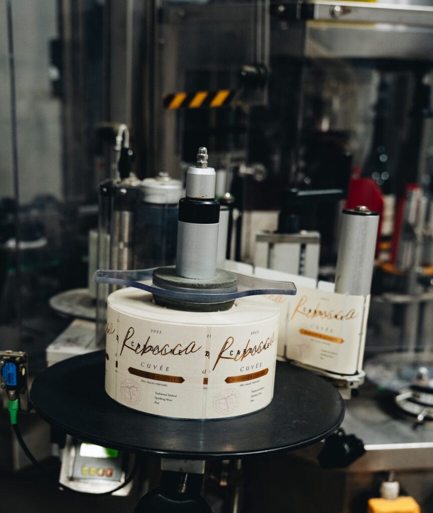 Rebecca Caroline labels being applied to sparkling wine bottles on the labeling line